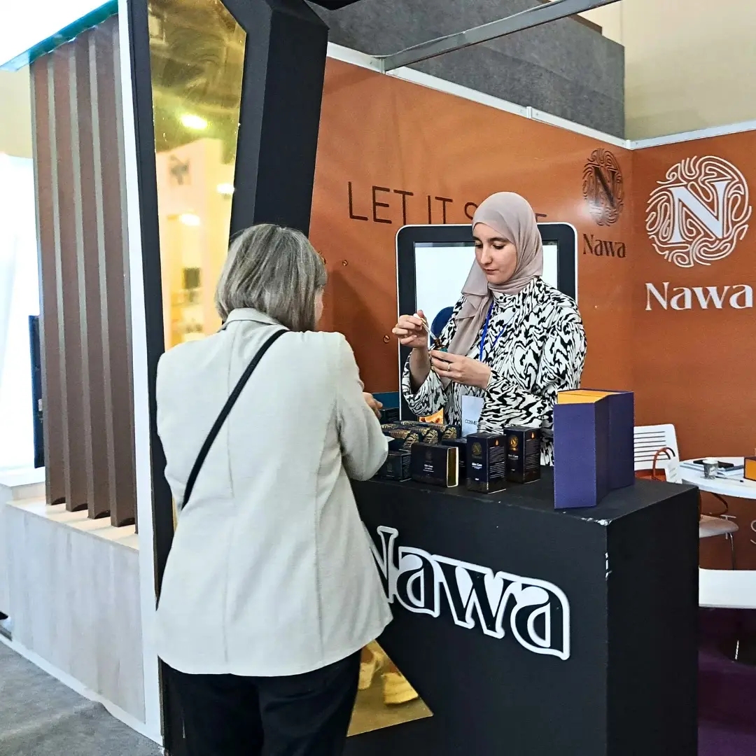 A visitor tries a product with an exhibitor at a brand's counter