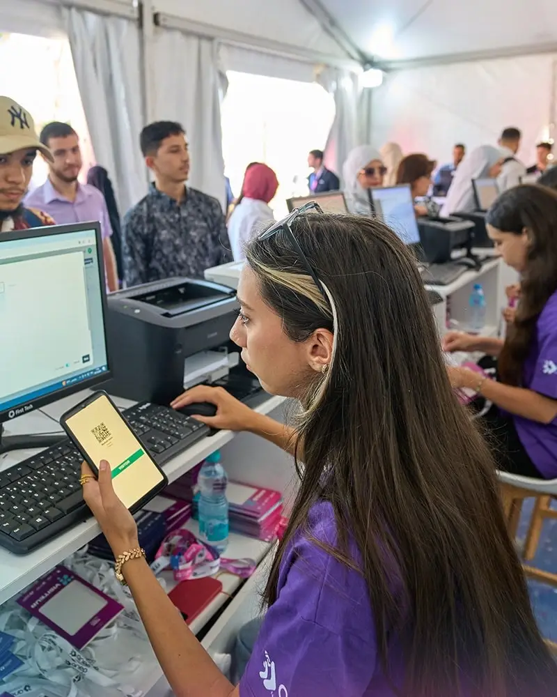 At the welcome desk, a hostess reads a visitor's QR code, with badges and a printer within reach